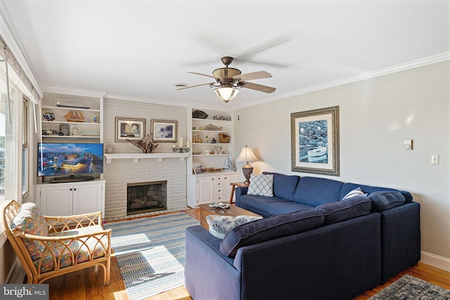 living room featuring hardwood / wood-style floors, ceiling fan, crown molding, a brick fireplace, and built in shelves