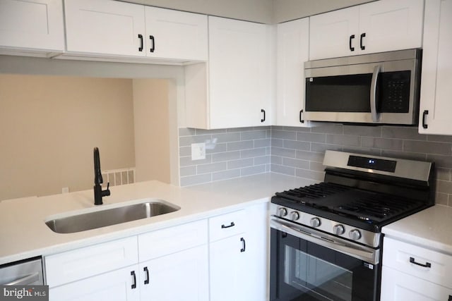 kitchen with tasteful backsplash, appliances with stainless steel finishes, sink, and white cabinets