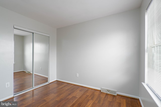 unfurnished bedroom featuring multiple windows, a closet, and dark hardwood / wood-style floors