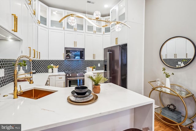 kitchen with sink, backsplash, high end appliances, light stone counters, and white cabinets