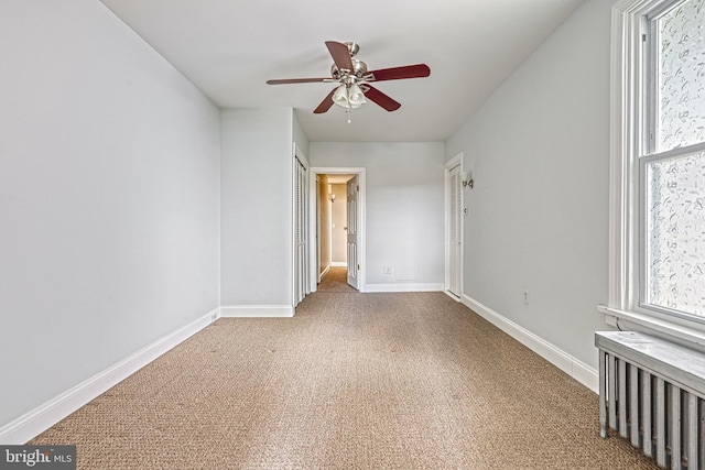 carpeted empty room featuring radiator and ceiling fan