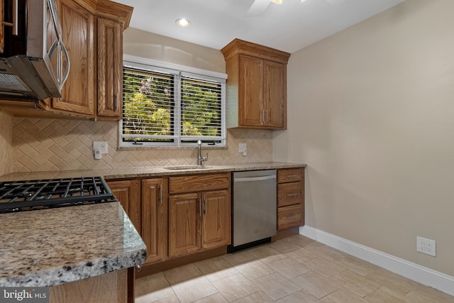 kitchen featuring stainless steel appliances, a sink, baseboards, brown cabinetry, and tasteful backsplash