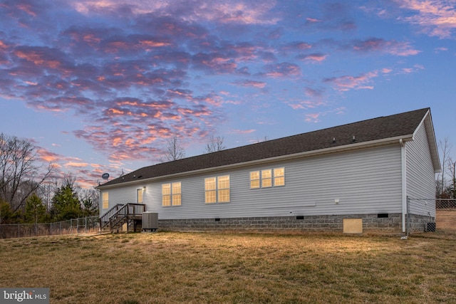 back house at dusk featuring central AC unit and a lawn