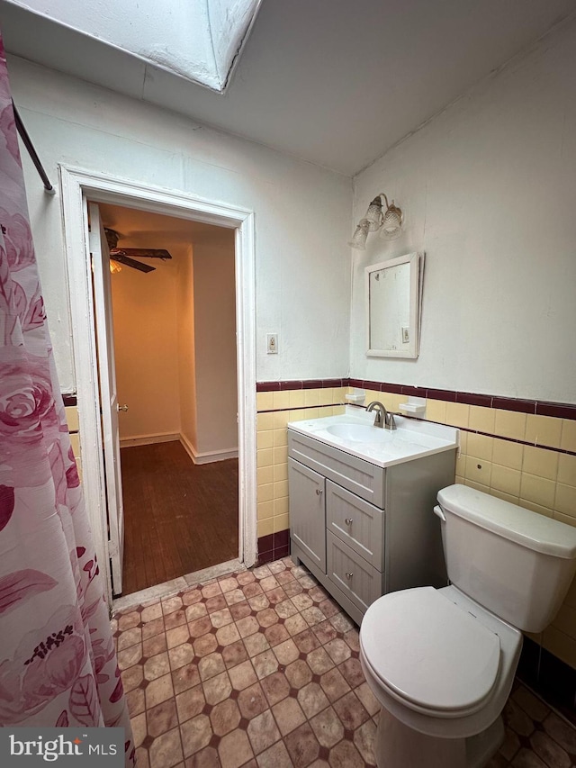 bathroom with a skylight, tile walls, vanity, ceiling fan, and toilet