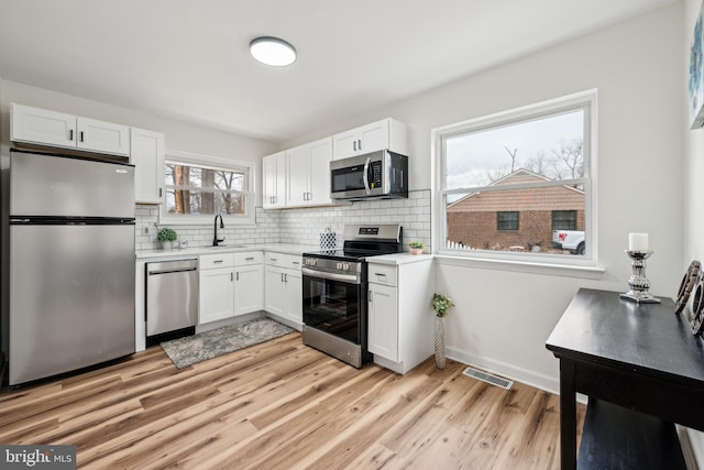 kitchen featuring light wood finished floors, stainless steel appliances, light countertops, visible vents, and white cabinetry