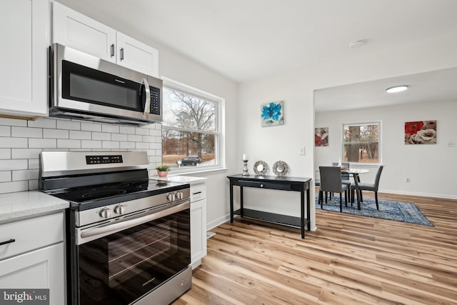 kitchen with a wealth of natural light, appliances with stainless steel finishes, tasteful backsplash, and light wood finished floors