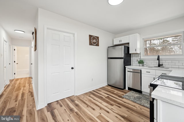 kitchen with a sink, decorative backsplash, light wood-style flooring, white cabinets, and appliances with stainless steel finishes
