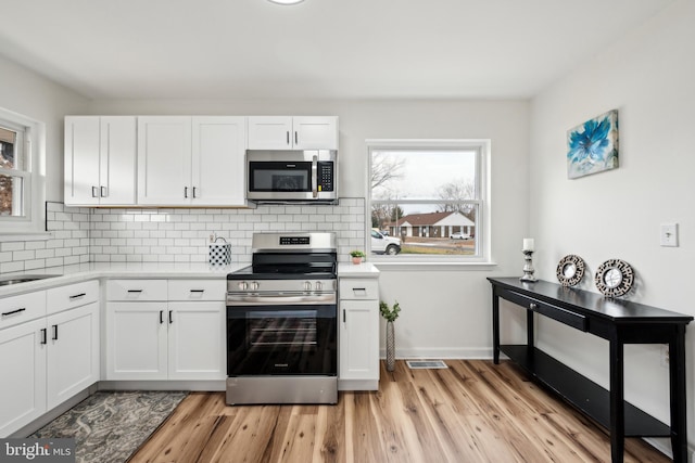 kitchen featuring stainless steel appliances, light countertops, light wood-type flooring, tasteful backsplash, and white cabinetry