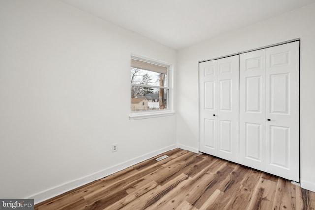 unfurnished bedroom with visible vents, baseboards, wood finished floors, and a closet
