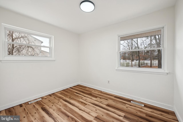 empty room featuring wood finished floors, visible vents, and baseboards