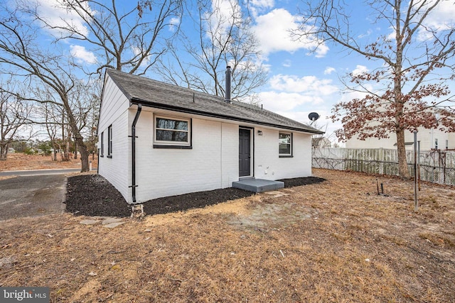 exterior space featuring fence, brick siding, and roof with shingles