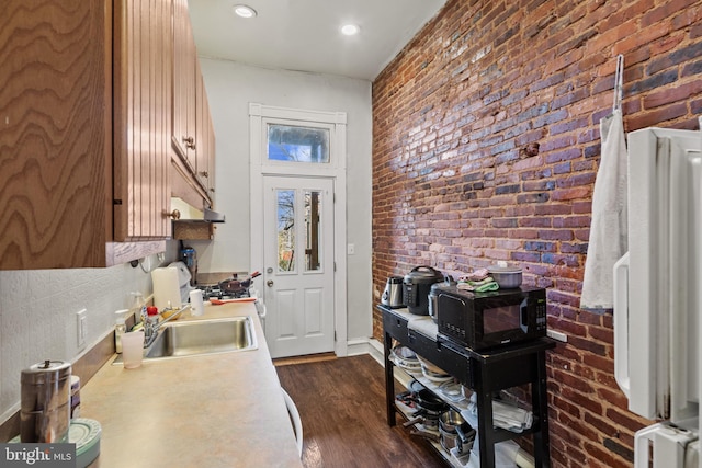 interior space with brick wall, dark hardwood / wood-style floors, sink, and a wood stove