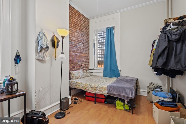 bedroom with hardwood / wood-style flooring, ornamental molding, and brick wall