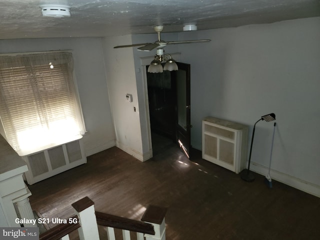 empty room with dark hardwood / wood-style flooring, radiator, heating unit, and ceiling fan