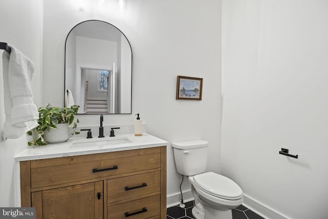 half bathroom featuring baseboards, vanity, toilet, and tile patterned floors