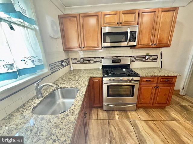 kitchen with sink, crown molding, appliances with stainless steel finishes, light stone counters, and tasteful backsplash