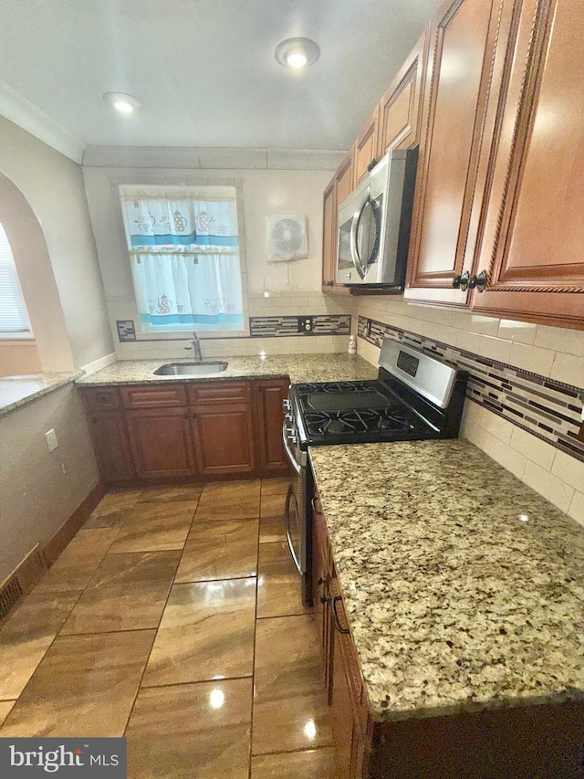 kitchen featuring appliances with stainless steel finishes, tasteful backsplash, sink, ornamental molding, and light stone counters