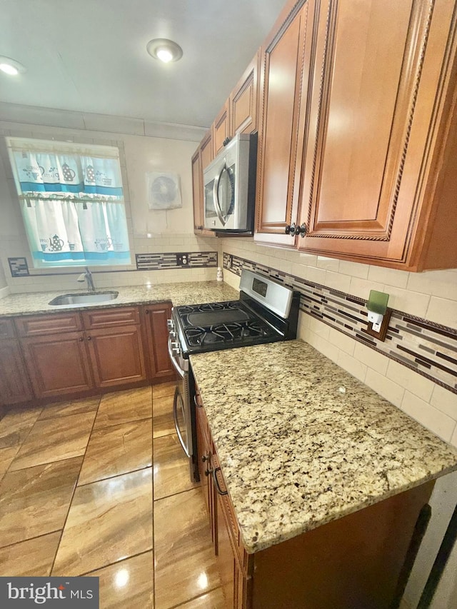 kitchen featuring light stone counters, sink, backsplash, and appliances with stainless steel finishes