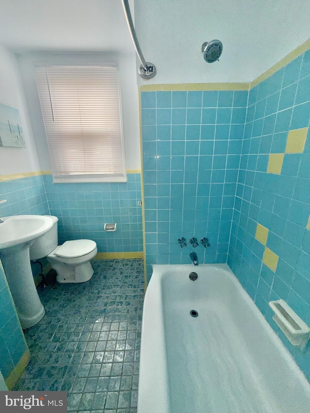 bathroom with tile patterned flooring, tiled shower / bath, tile walls, and toilet