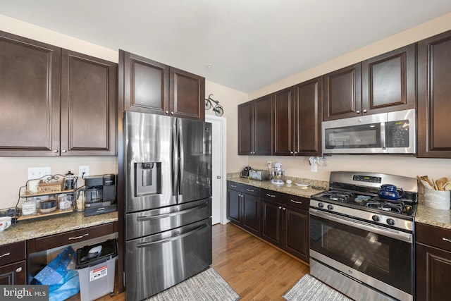 kitchen featuring stainless steel appliances, dark brown cabinets, light stone counters, and light wood-style floors