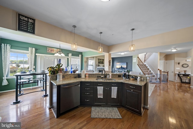 kitchen with wood finished floors, a sink, open floor plan, hanging light fixtures, and dishwasher