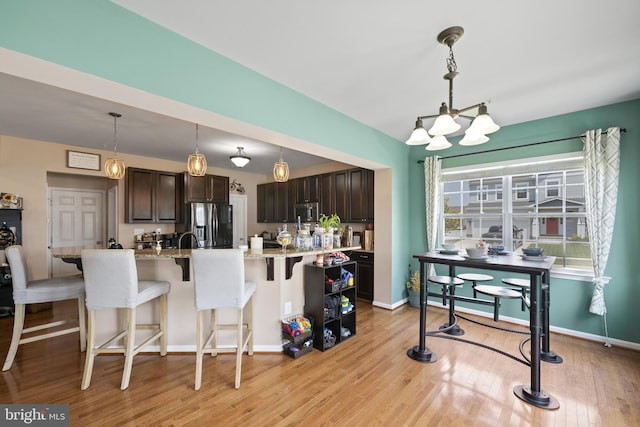 kitchen featuring stainless steel appliances, hanging light fixtures, dark brown cabinetry, and light stone counters