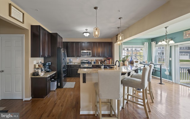 kitchen featuring a kitchen island with sink, appliances with stainless steel finishes, pendant lighting, and light stone counters