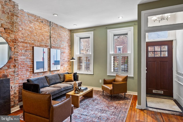 living area with brick wall, visible vents, baseboards, and hardwood / wood-style flooring