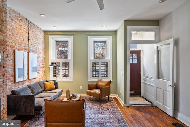 sitting room featuring hardwood / wood-style flooring, brick wall, baseboards, and a ceiling fan