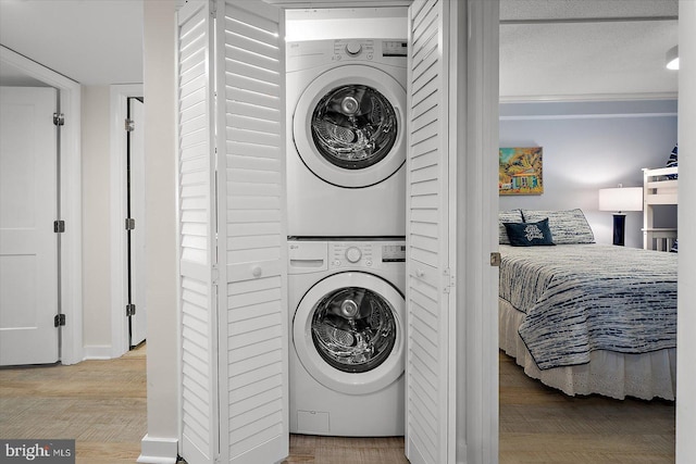 laundry area featuring crown molding, stacked washer / drying machine, and light hardwood / wood-style floors