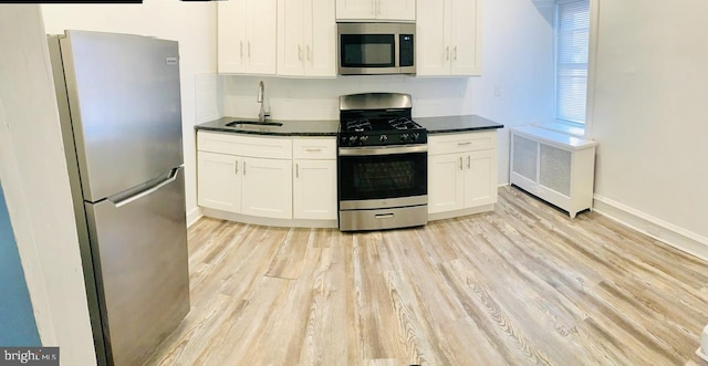 kitchen with appliances with stainless steel finishes, radiator heating unit, sink, and white cabinets