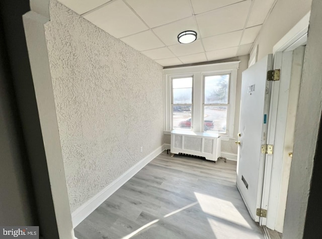 hall featuring light hardwood / wood-style flooring, radiator, and a paneled ceiling