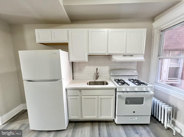 kitchen with radiator heating unit, sink, light wood-type flooring, white cabinets, and white appliances