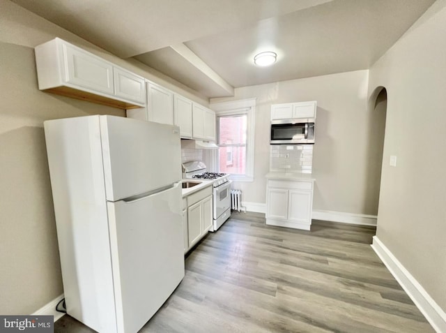 kitchen with radiator, white appliances, white cabinets, decorative backsplash, and light wood-type flooring