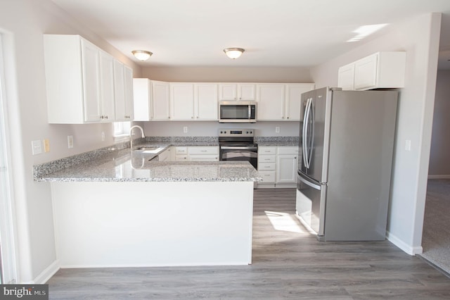 kitchen with sink, stainless steel appliances, light stone counters, white cabinets, and kitchen peninsula