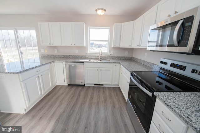 kitchen with sink, light stone counters, light hardwood / wood-style flooring, stainless steel appliances, and white cabinets