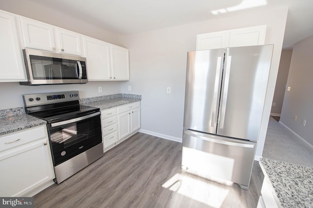 kitchen with white cabinetry, appliances with stainless steel finishes, light wood-type flooring, and light stone counters