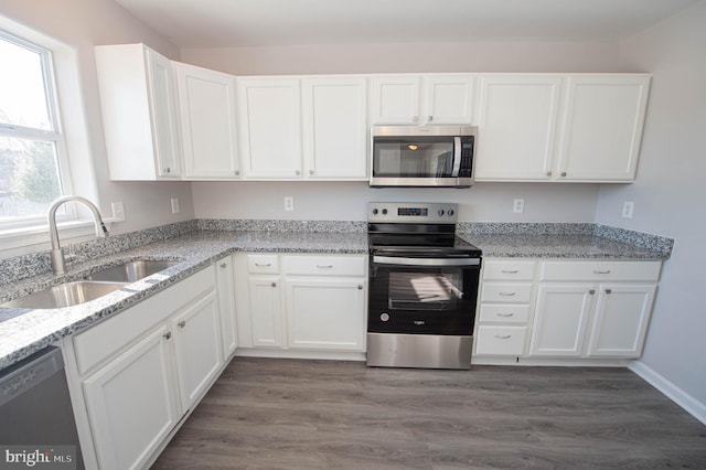 kitchen featuring appliances with stainless steel finishes, white cabinetry, sink, light stone counters, and dark wood-type flooring