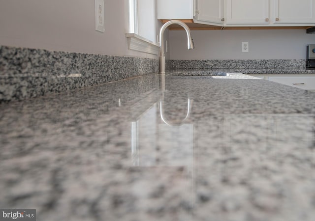 interior details featuring white cabinetry, sink, and stone countertops