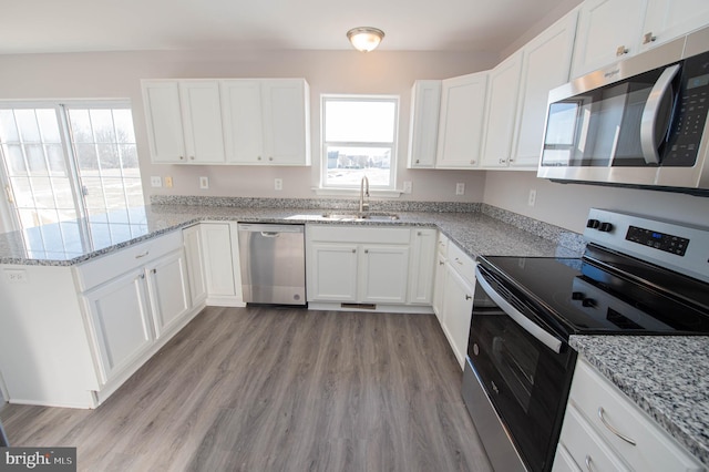 kitchen featuring appliances with stainless steel finishes, sink, white cabinets, light stone counters, and light wood-type flooring