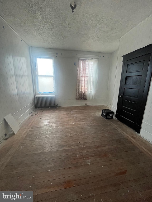 interior space with dark wood-type flooring, radiator heating unit, a textured ceiling, and wood walls