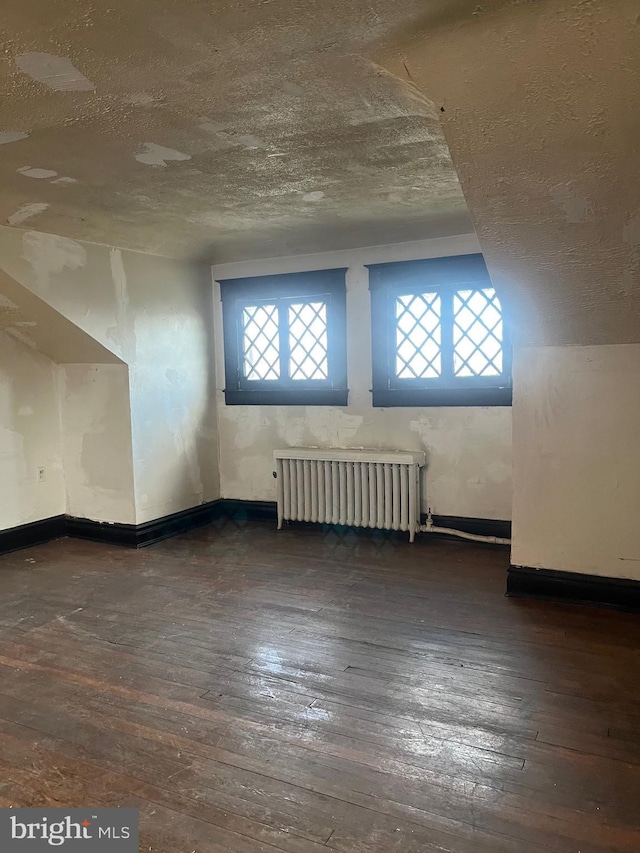 bonus room featuring dark wood-type flooring, radiator heating unit, and a textured ceiling