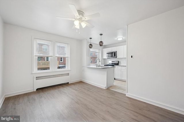 kitchen featuring appliances with stainless steel finishes, pendant lighting, radiator heating unit, white cabinetry, and kitchen peninsula