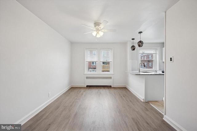 unfurnished living room featuring light hardwood / wood-style flooring, sink, radiator heating unit, and ceiling fan