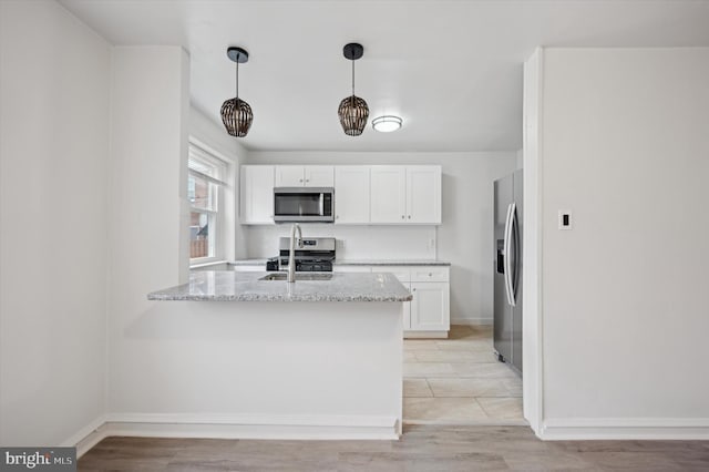 kitchen with sink, white cabinetry, stainless steel appliances, light stone counters, and decorative light fixtures