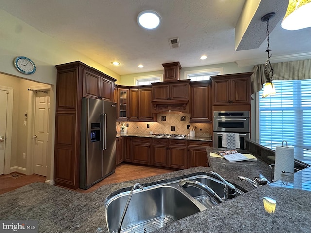 kitchen with sink, dark stone counters, pendant lighting, stainless steel appliances, and decorative backsplash