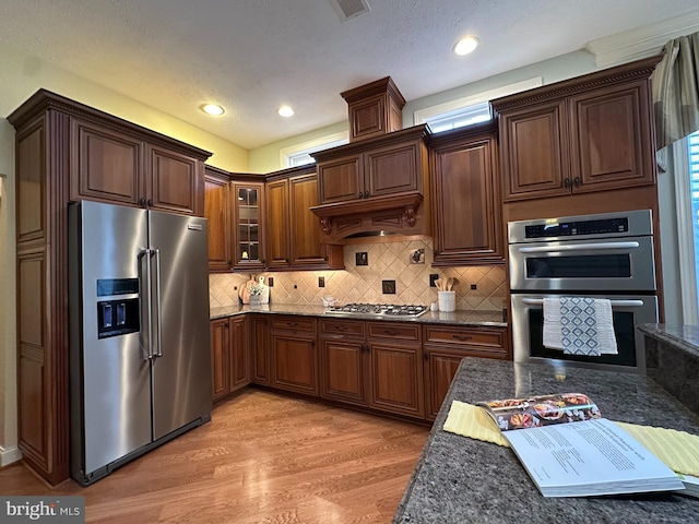 kitchen with appliances with stainless steel finishes, dark stone countertops, backsplash, and light wood-type flooring