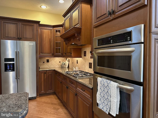 kitchen featuring appliances with stainless steel finishes, dark stone countertops, backsplash, and light hardwood / wood-style floors