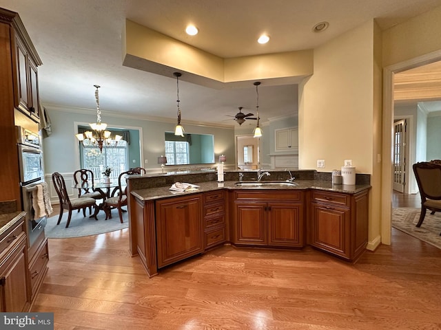 kitchen featuring sink, hanging light fixtures, light wood-type flooring, ornamental molding, and kitchen peninsula