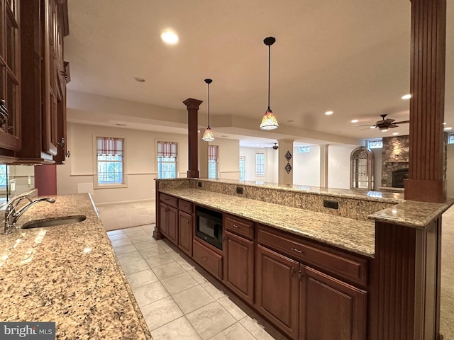 kitchen featuring sink, black microwave, pendant lighting, ceiling fan, and light stone countertops